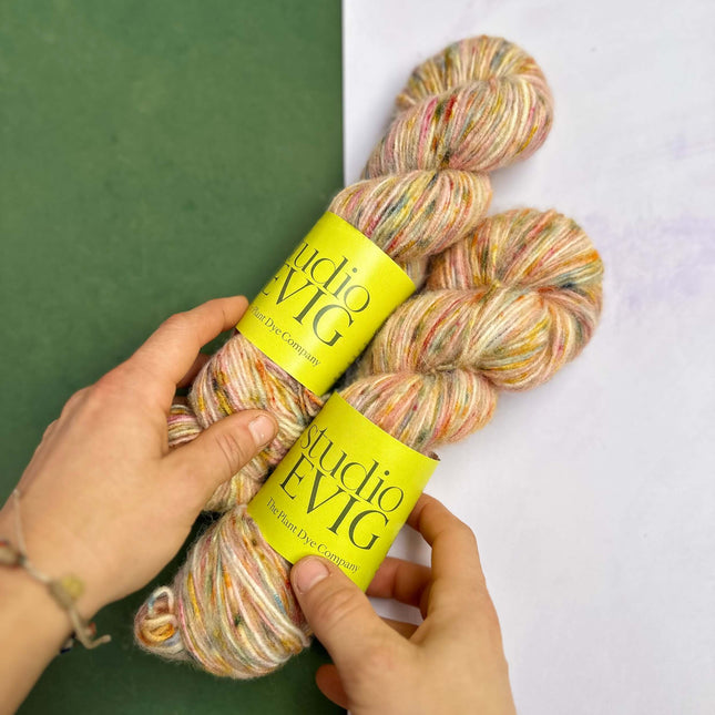 Colorful 'birthday cake' yarn skeins with yellow labels held by a hand on a green and white background