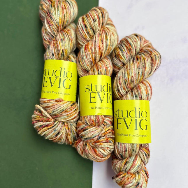 Three skeins of multicolored 'birthday cake' yarn with 'studio EVIG' labels on a green and white background.
