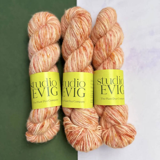 Three skeins of peach-colored yarn with 'studio EVIG' labels on a green and white background.