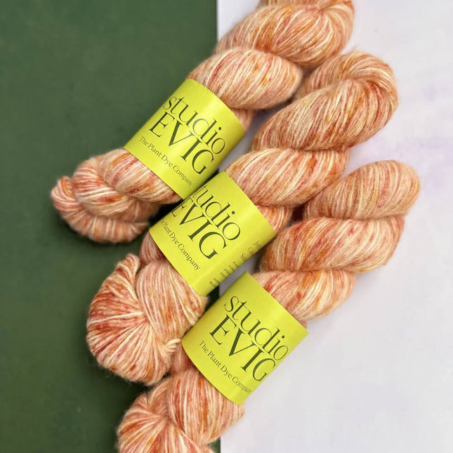 Three skeins of yarn with 'Studio EVIG' labels on a green and white background