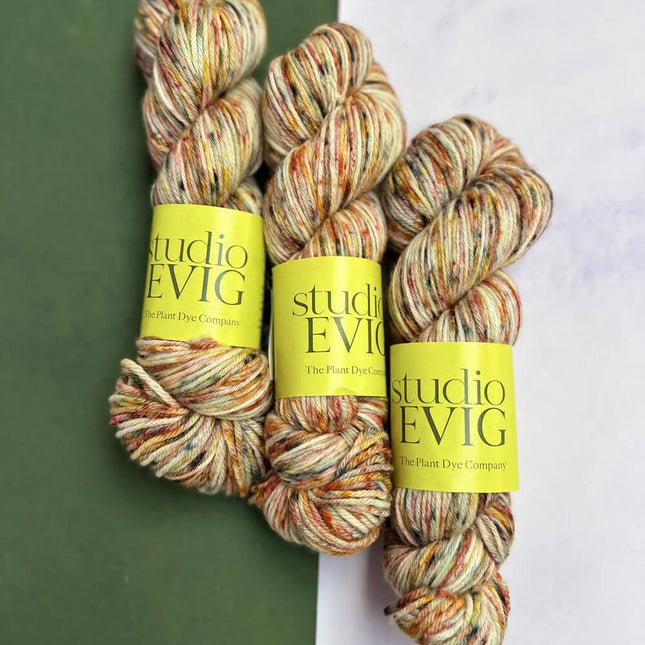 Three skeins of yarn with 'studio EVIG' labels on a green and white background