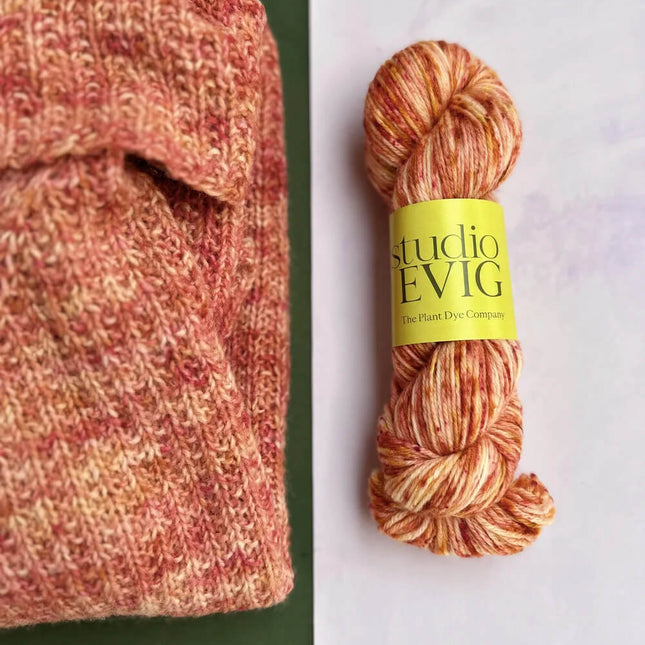 Yarn skein with a studio EVIG label next to a knitted fabric on a green and white background